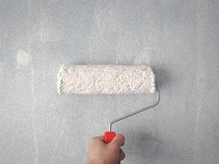 Paint roller applying white paint to a wall